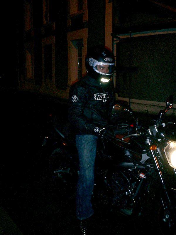 Cadrage vertical : le pilote de profil sur la moto, à l’arrêt dans la nuit.