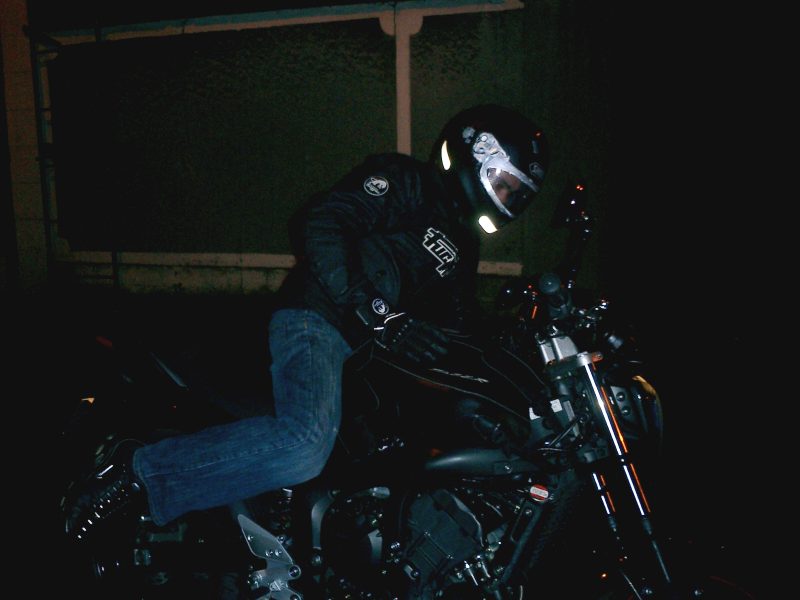 Le pilote assis en selle, vu de côté, dans la pénombre.