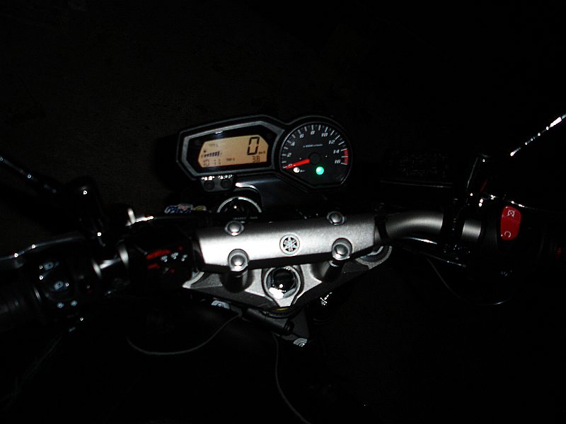 Le poste de pilotage vu depuis la selle : compteur et compte-tours allumés, guidon large, té supérieur marqué Yamaha.