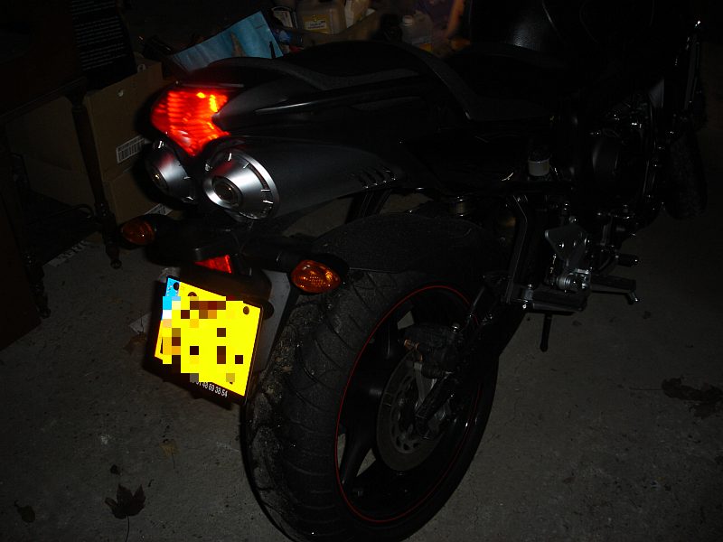 L’arrière de la moto dans la pénombre du garage, feu rouge allumé.